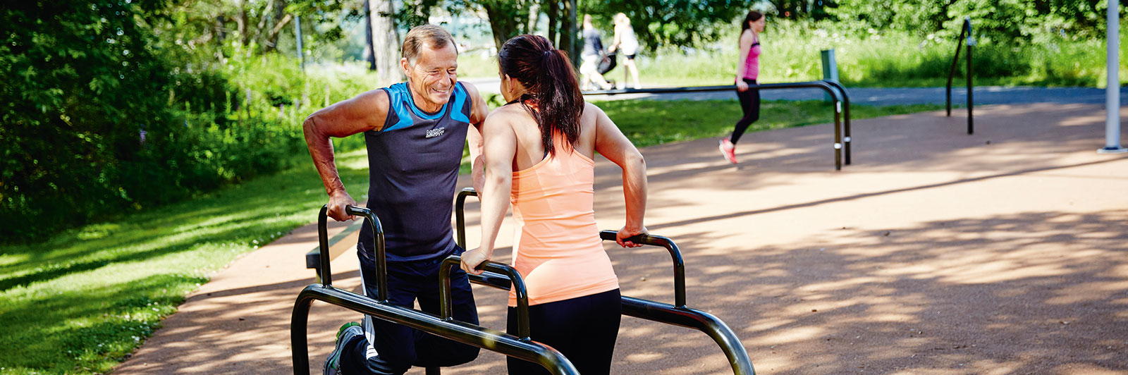 A man and woman exercise on dip bars at the same time, they are at different heights with adjusted difficulty level.